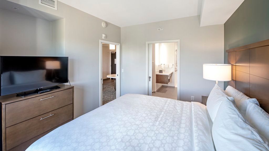 image The bedroom displays a king bed with white linens, bedside tables, a dresser with a television, and a doorway leading to the bathroom.
