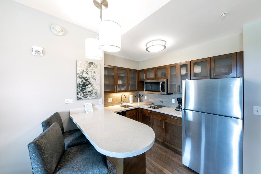 image The kitchen includes dark wood cabinets, stainless steel appliances, a refrigerator, and a bar counter with seating.