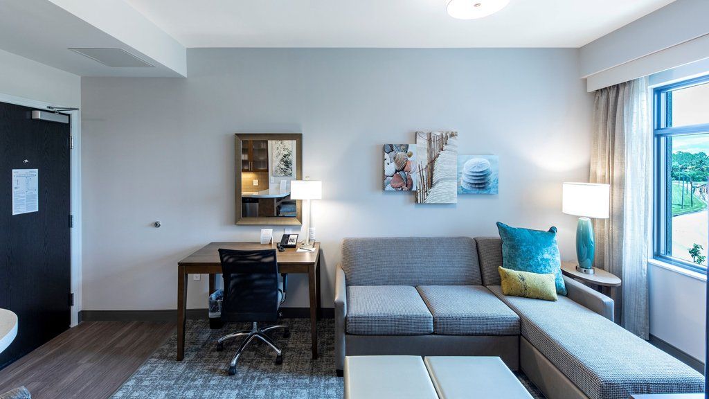 image The living area features a sofa, a wooden desk with a chair, a lamp, decorative wall art, and a large window.