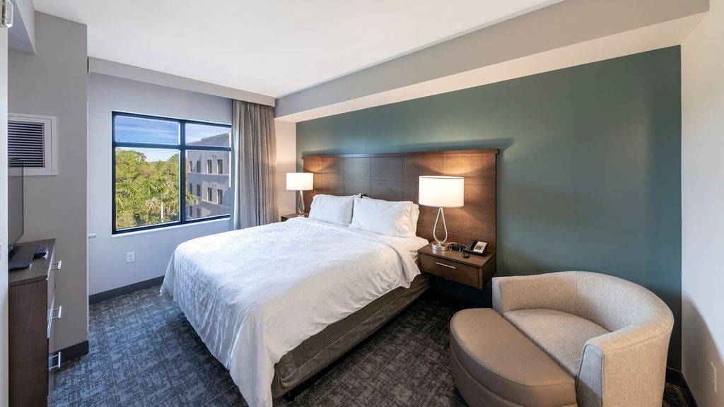 image The bedroom shows a queen bed with white linens, bedside tables with lamps, a window, and a chair positioned near the wall.