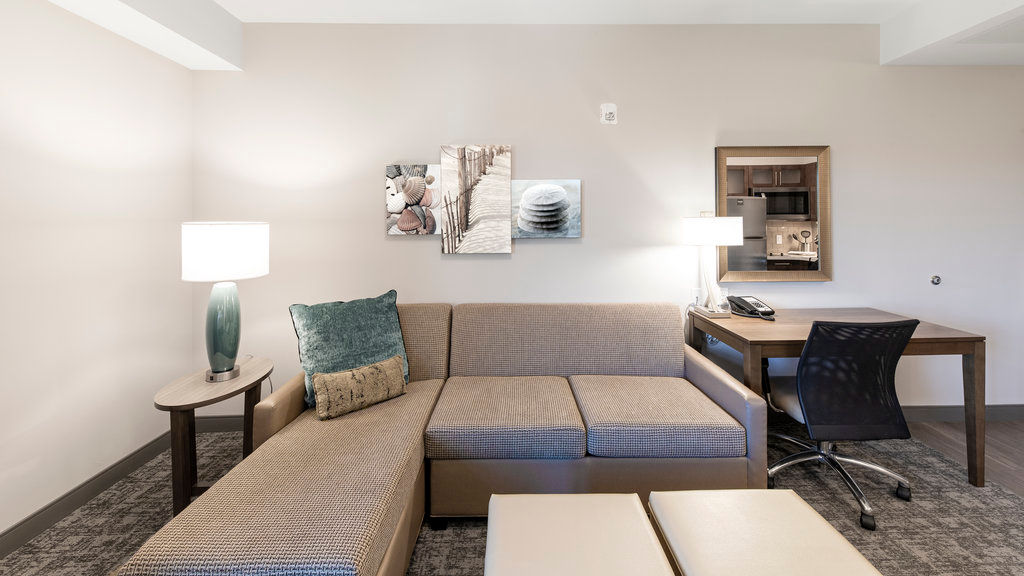 image Unwind in a seating area with a sectional sofa, a lamp, and a small round table beside the kitchenette.