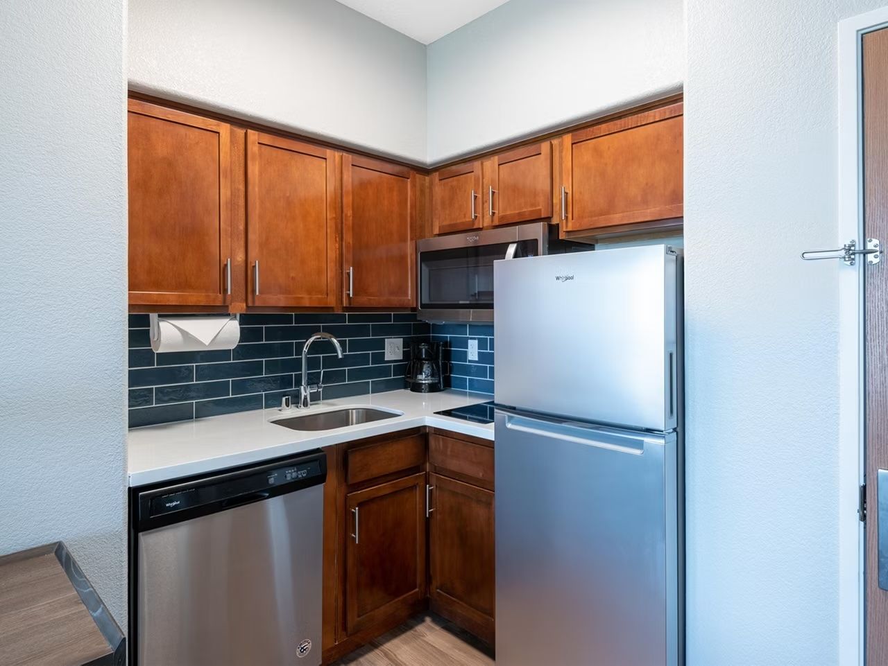 image Full kitchen with wood cabinetry, stainless fridge, dishwasher, microwave, and blue tile backsplash