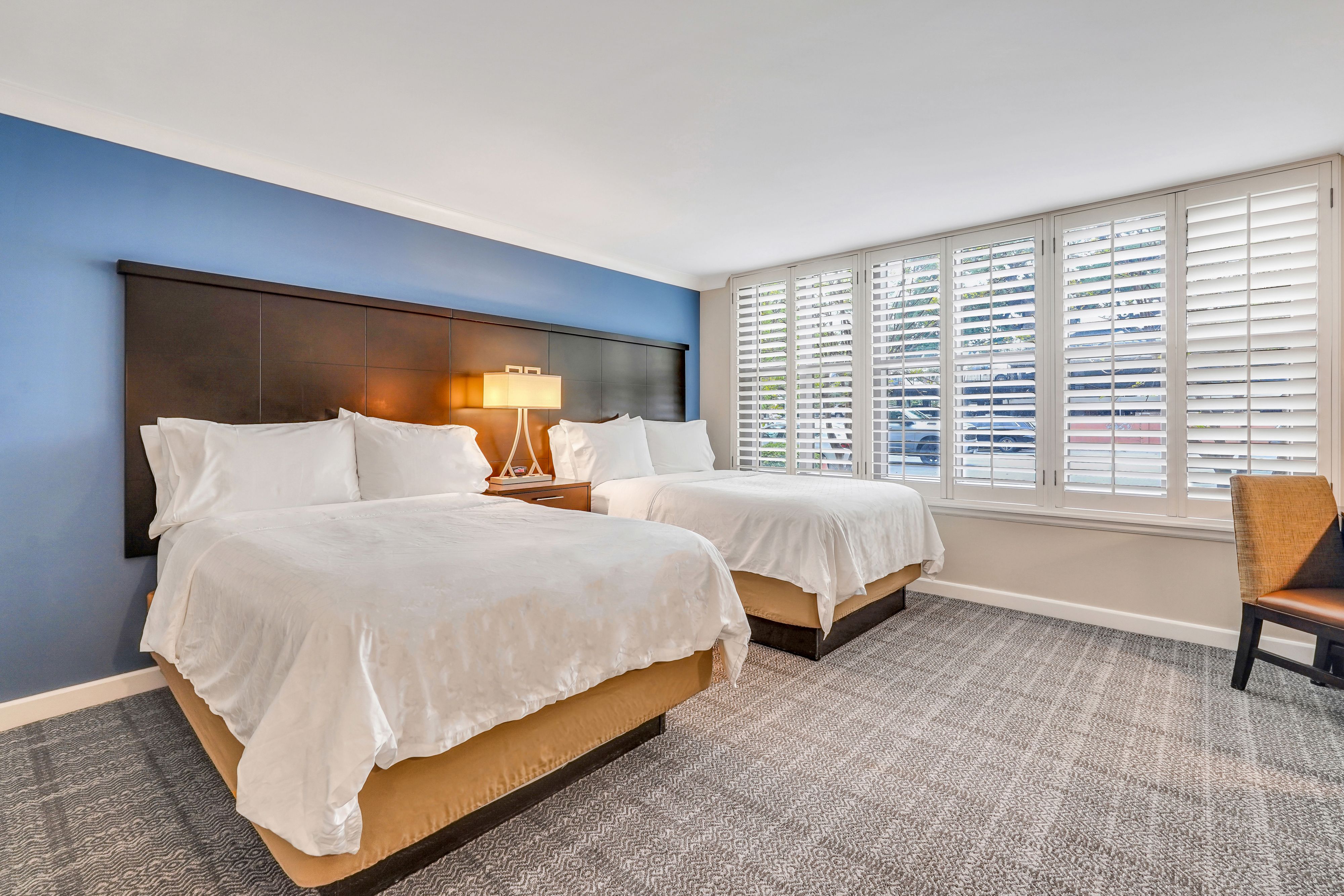 image Two double beds with soft white linens, warm wood floors, and accessible layout.