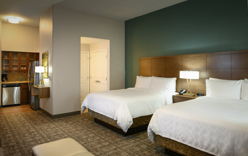 image Two queen beds beside a kitchen with modern appliances and bright accent lighting.