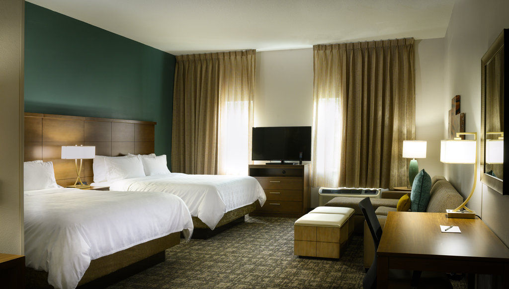 image The studio features two queen beds with warm-toned decor, a flat-screen TV, and a cozy seating area beside large windows.