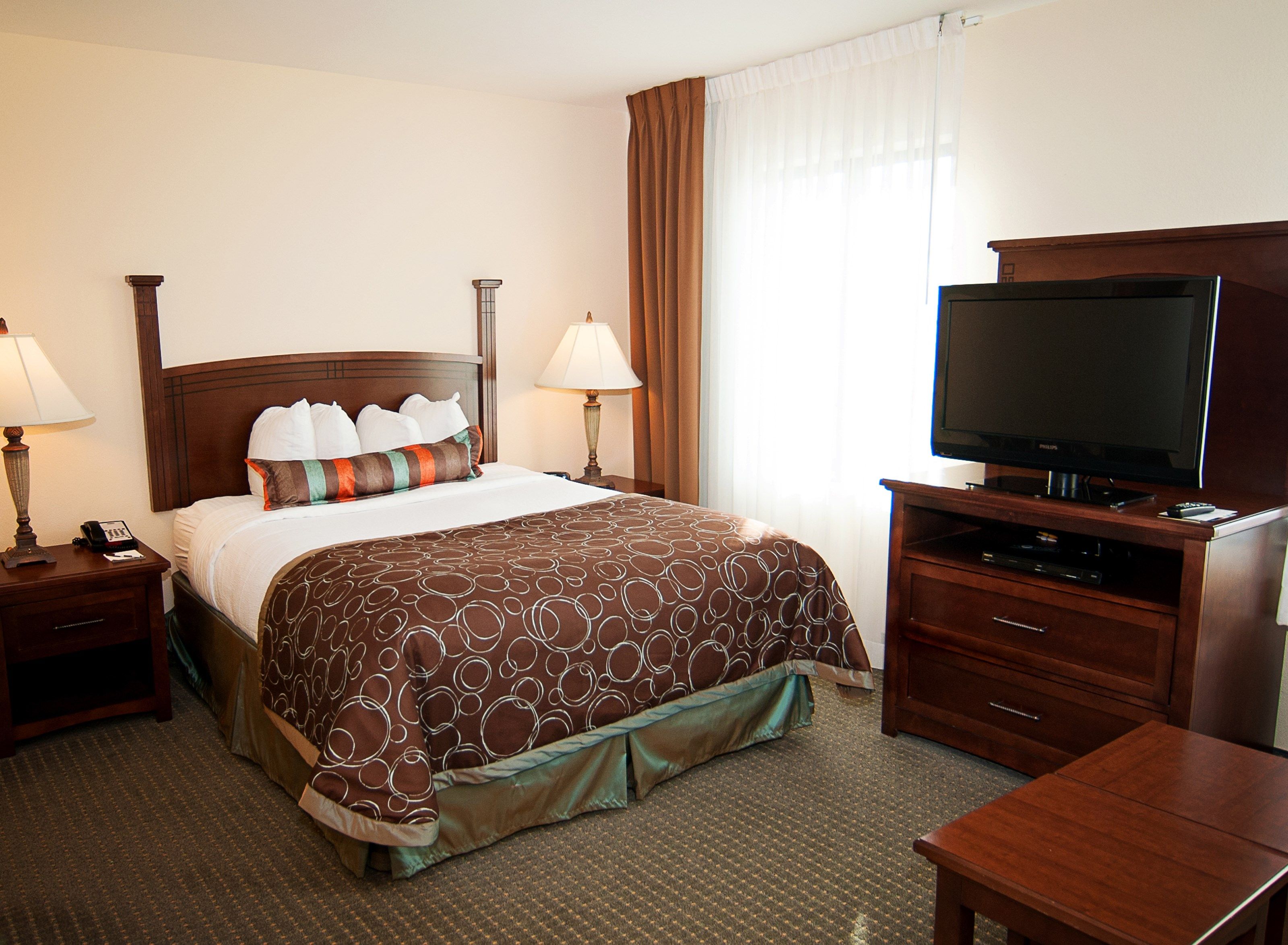 image Queen bed with patterned brown bedspread, bedside lamps, and flatscreen TV on the wooden dresser