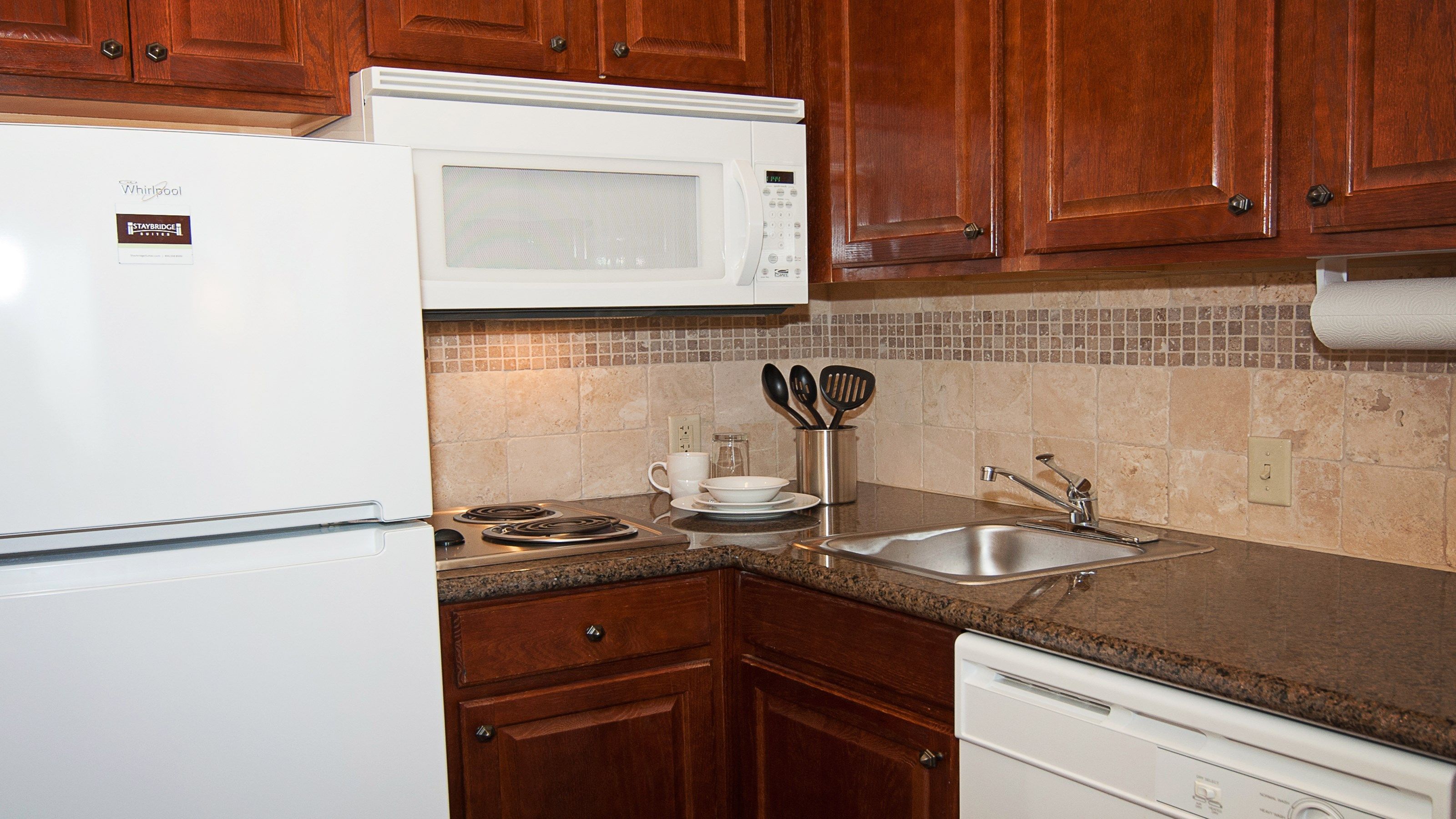 image Dark wood cabinetry with refrigerator, built-in microwave, electric stove, dishwasher, and stainless steel sink