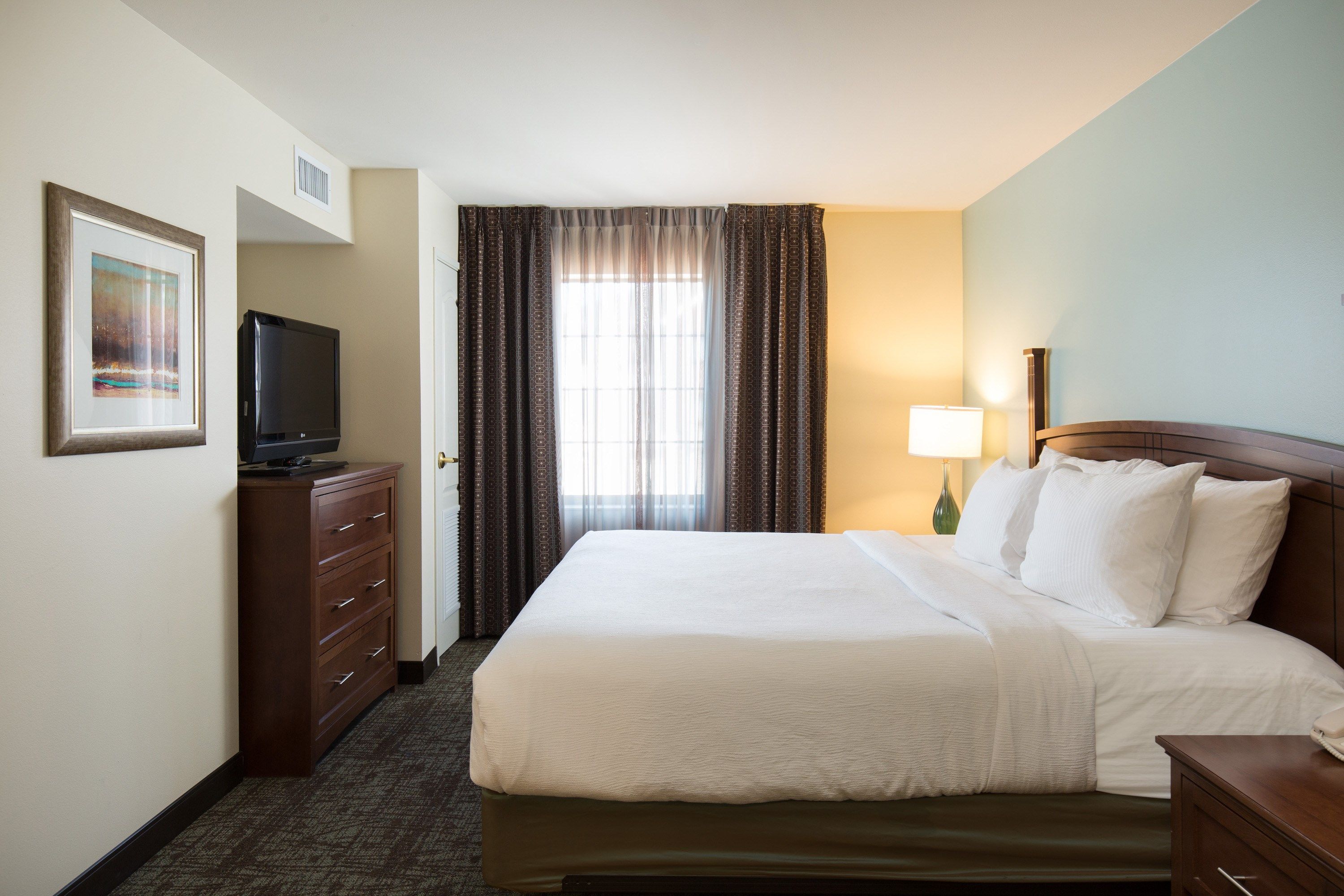 image King bed with white duvet and a reading lamp on each side — blackout curtains block the morning light