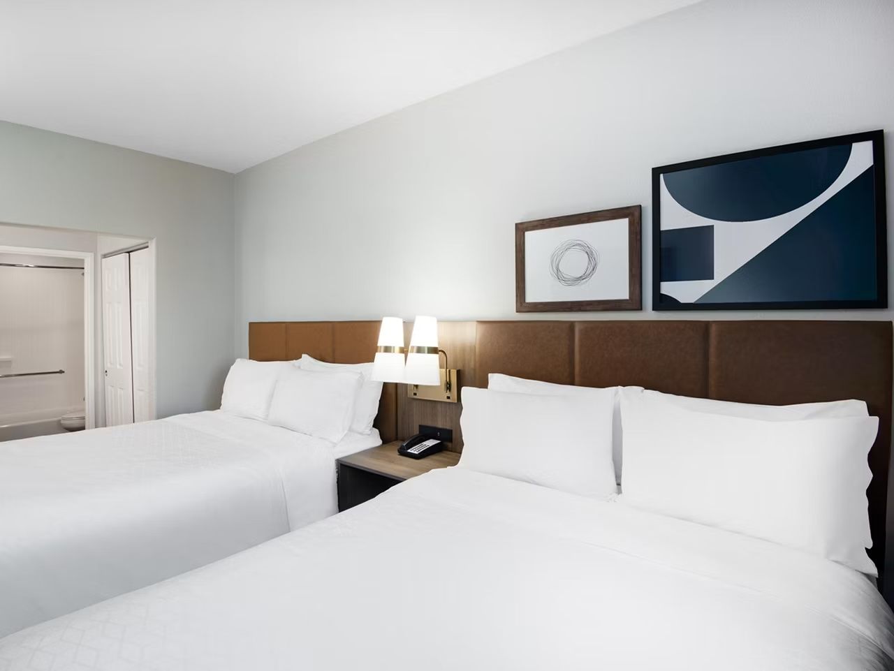 image Two queen beds with framed artwork above and a lamp on each nightstand