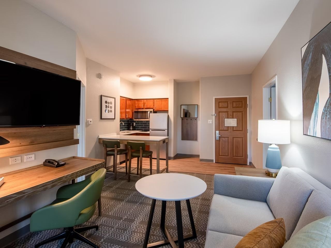 image Living area with gray sofa, work desk, flat-screen TV, and kitchen with dining bar in view