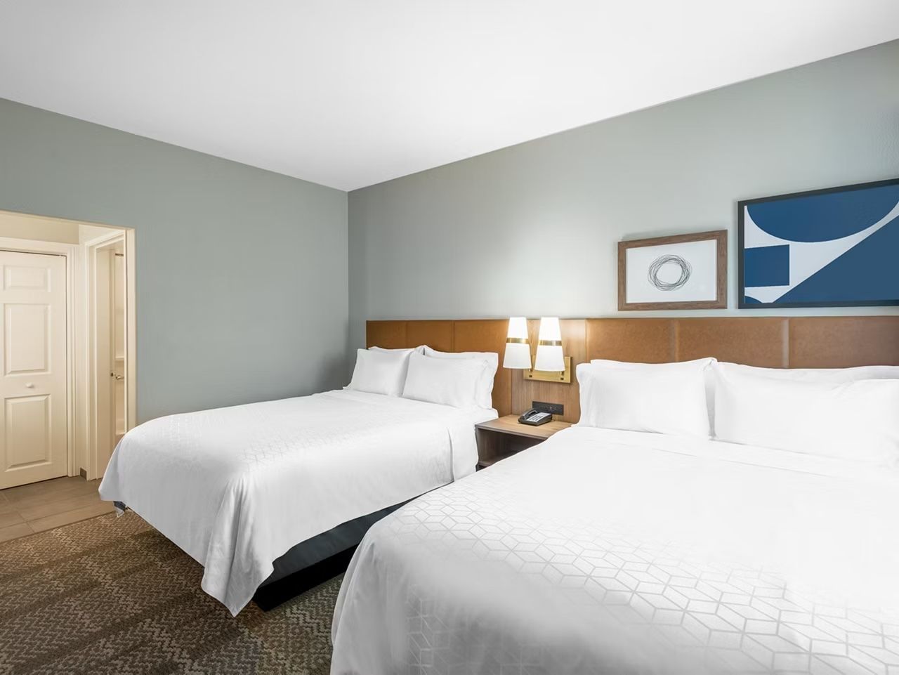image Two queen beds with white linens, a shared nightstand, and a wall-mounted flat-screen TV