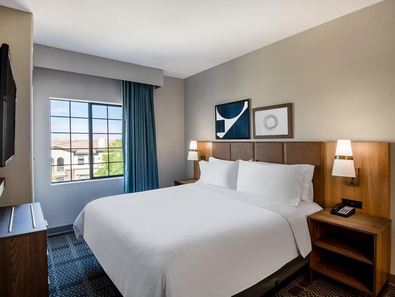 image King bed with white linens, wood nightstands, flat-screen TV, and blue curtains
