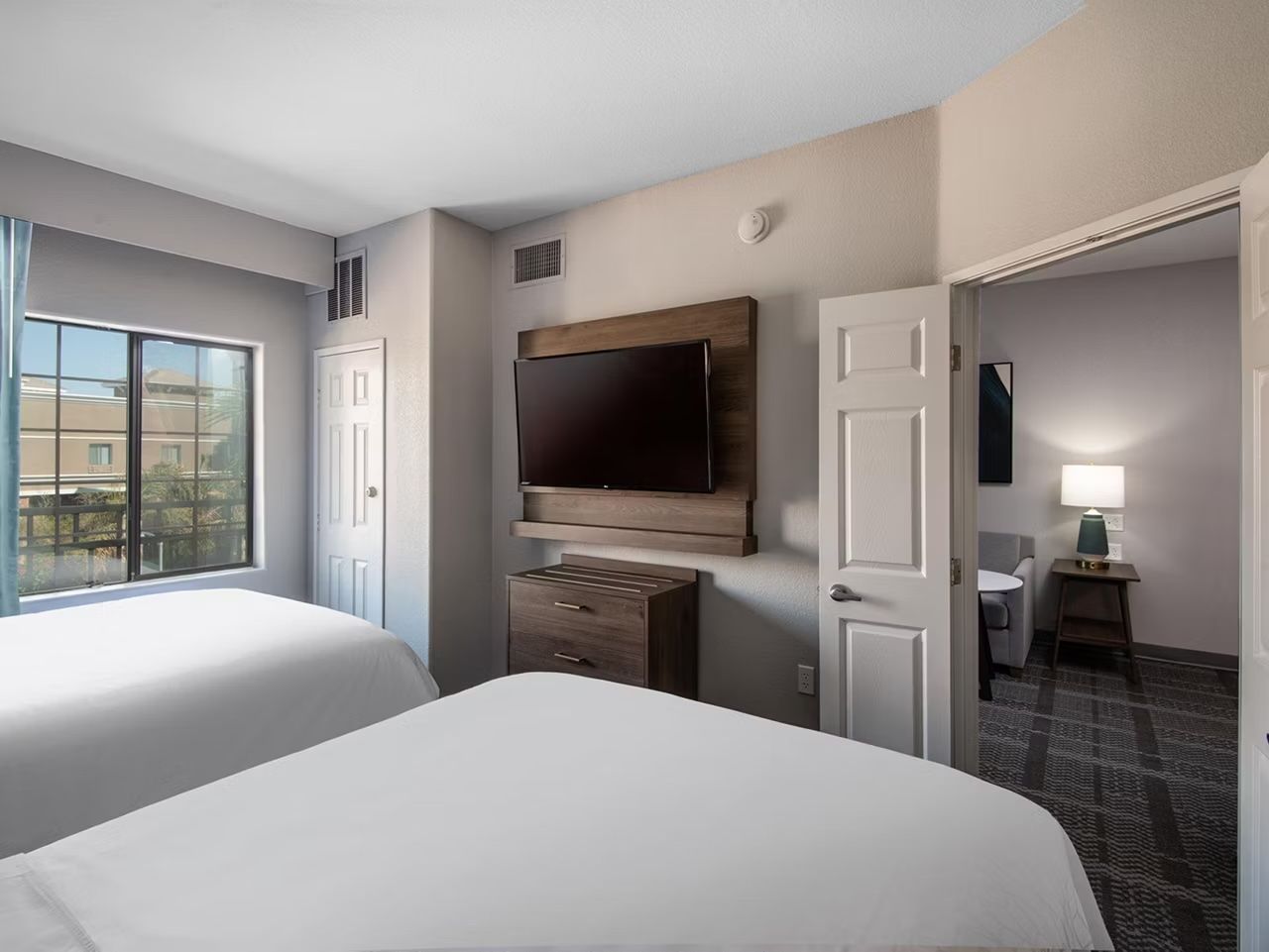 image Queen bed with wall-mounted TV, desk lamp, and window — a restful retreat after a day at Desert Diamond Arena