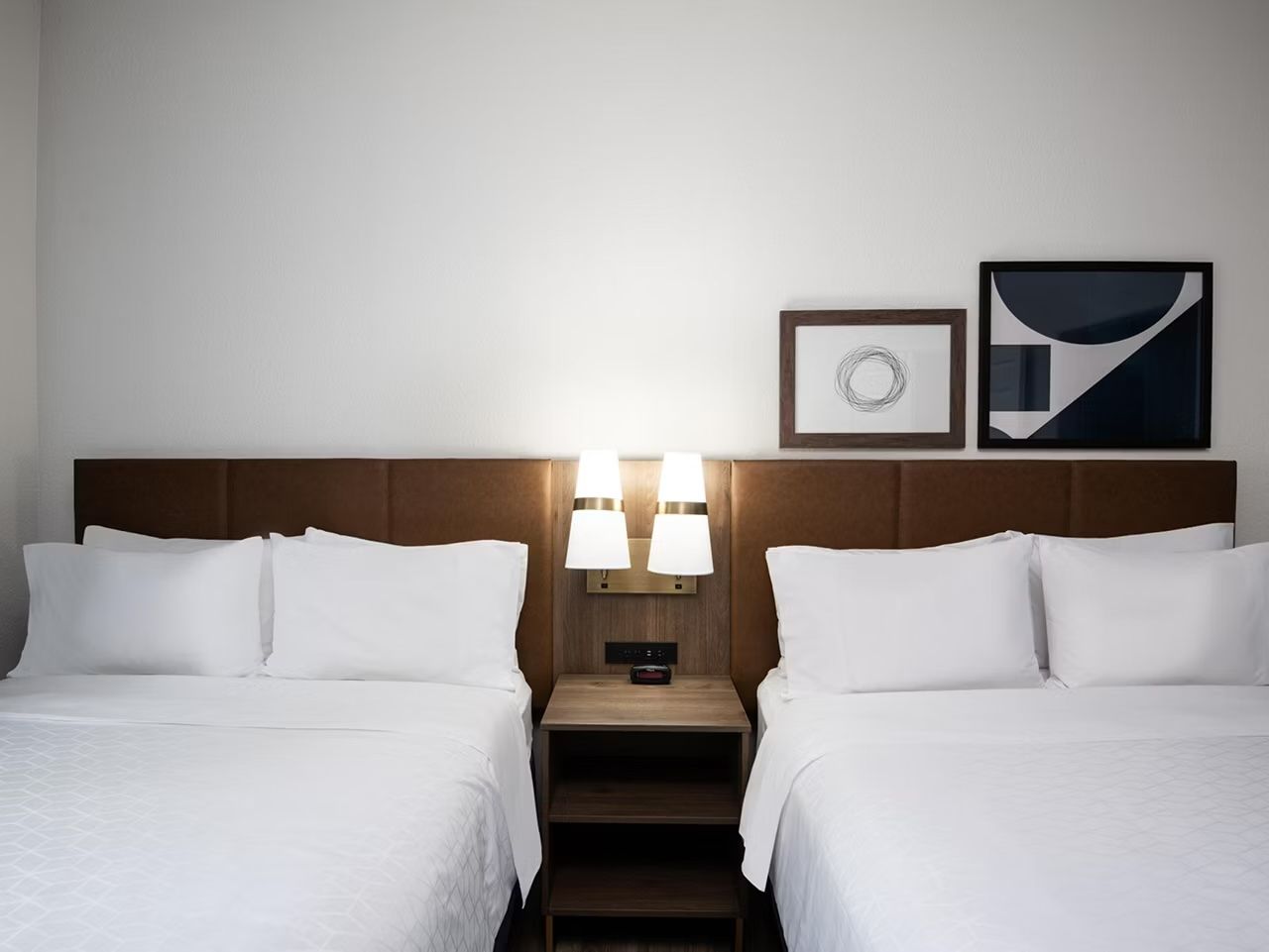 image Two queen beds with crisp white linens, wood headboards, and bedside lamps on each side