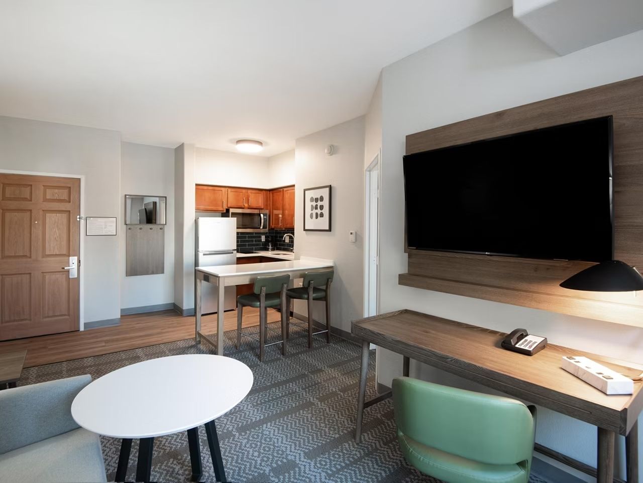image Open living and dining area with a full-size TV, work desk, dining table, and kitchen visible in the background