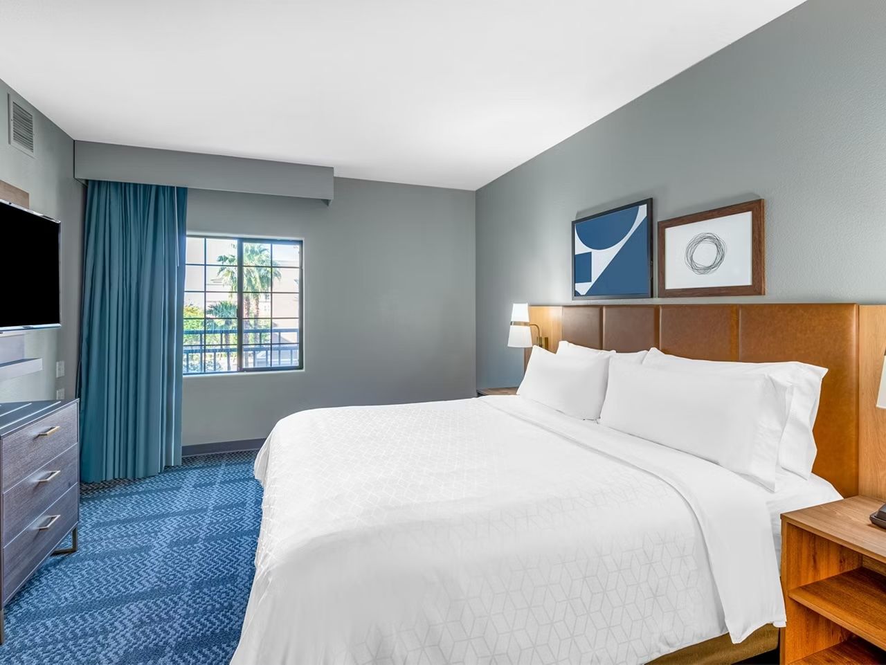 image King bed with light blue curtains and a flat-screen TV mounted on the opposite wall