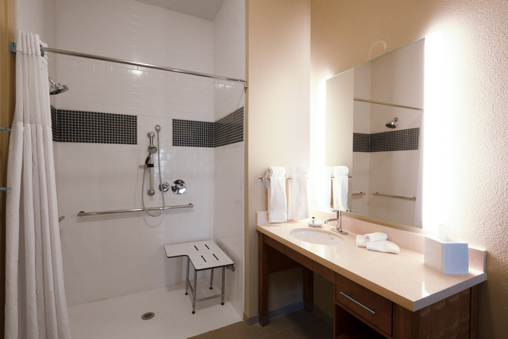 image Accessible walk-in shower with white and black tile, foldable seat, grab bars, and a modern round basin sink