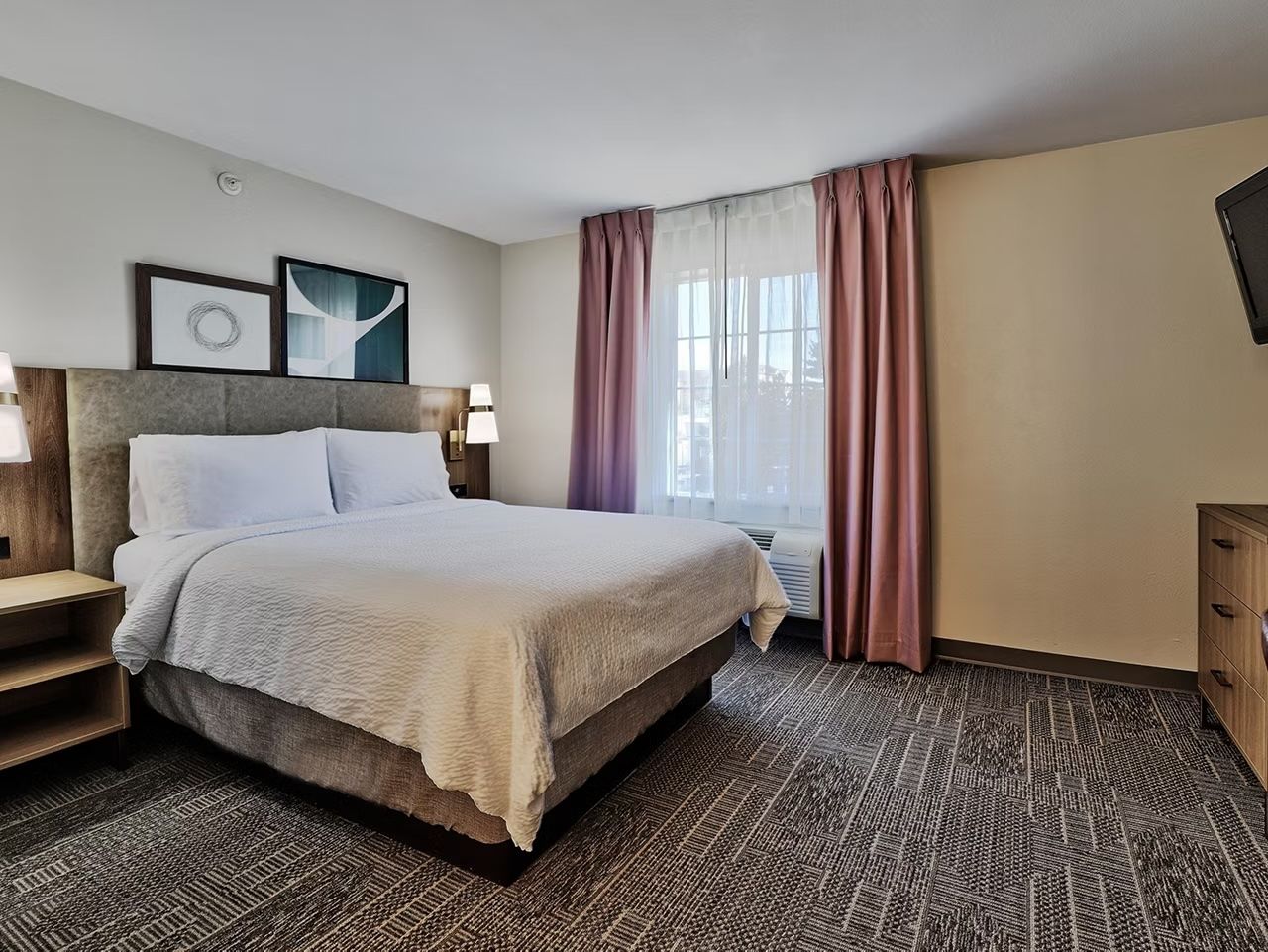 image King bed with soft white linens and natural light — flat-screen TV and clothing storage also in the room