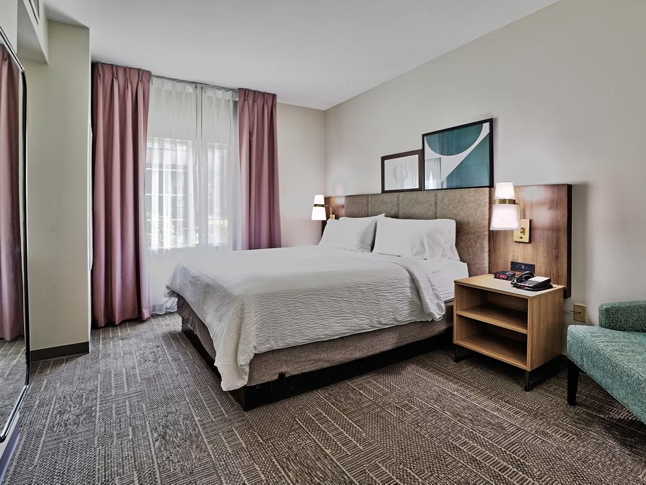 image Queen bed with warm-toned linens and natural light filtering through the curtains — dedicated workspace just off to the side