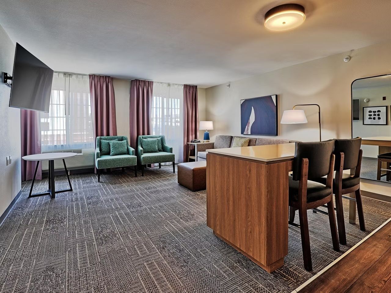 image Meeting table with seating for small groups sits alongside a sofa and flat-screen TV — sunlight comes in through the curtains