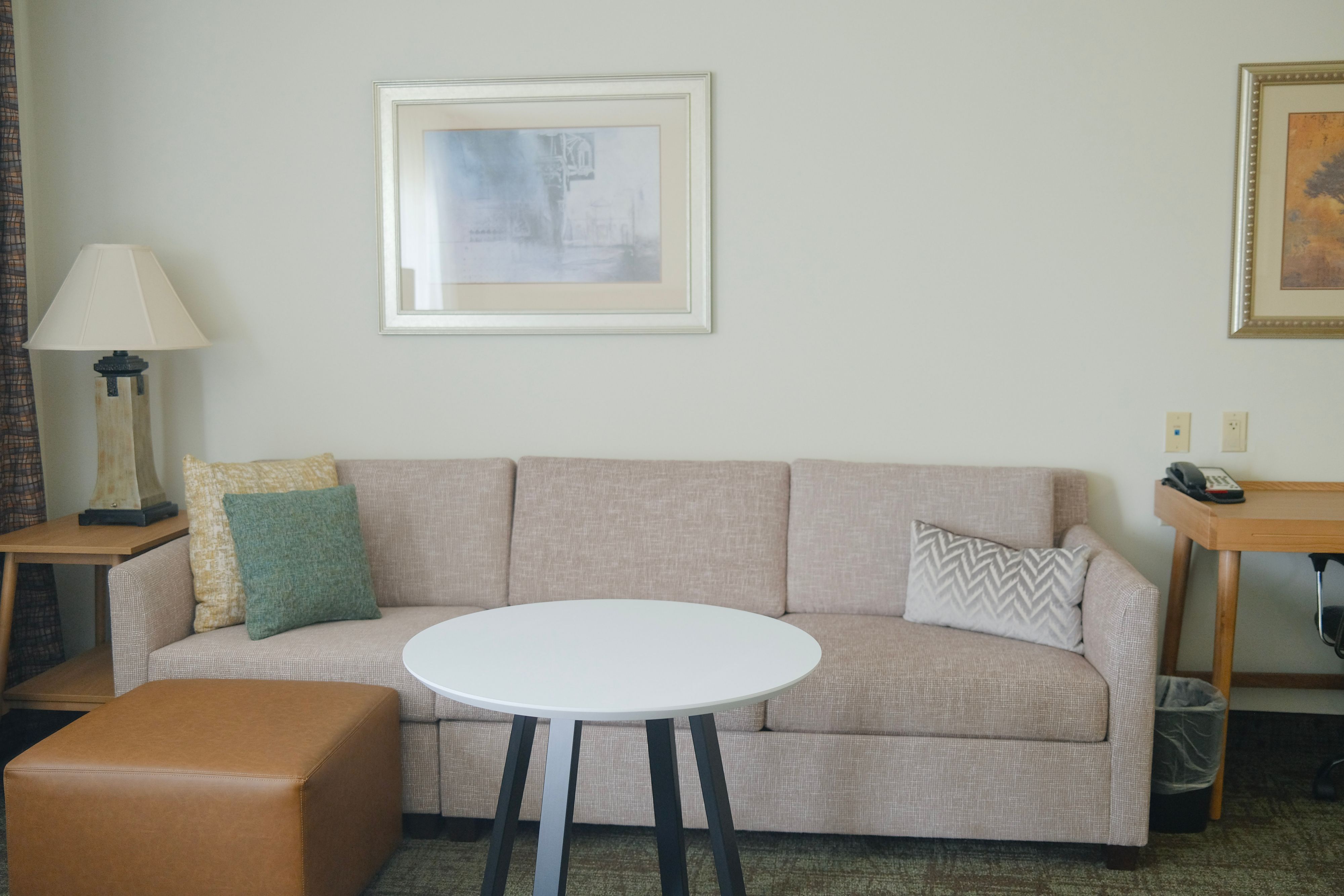 image Living area with sofa, round table, lamp, and artwork.