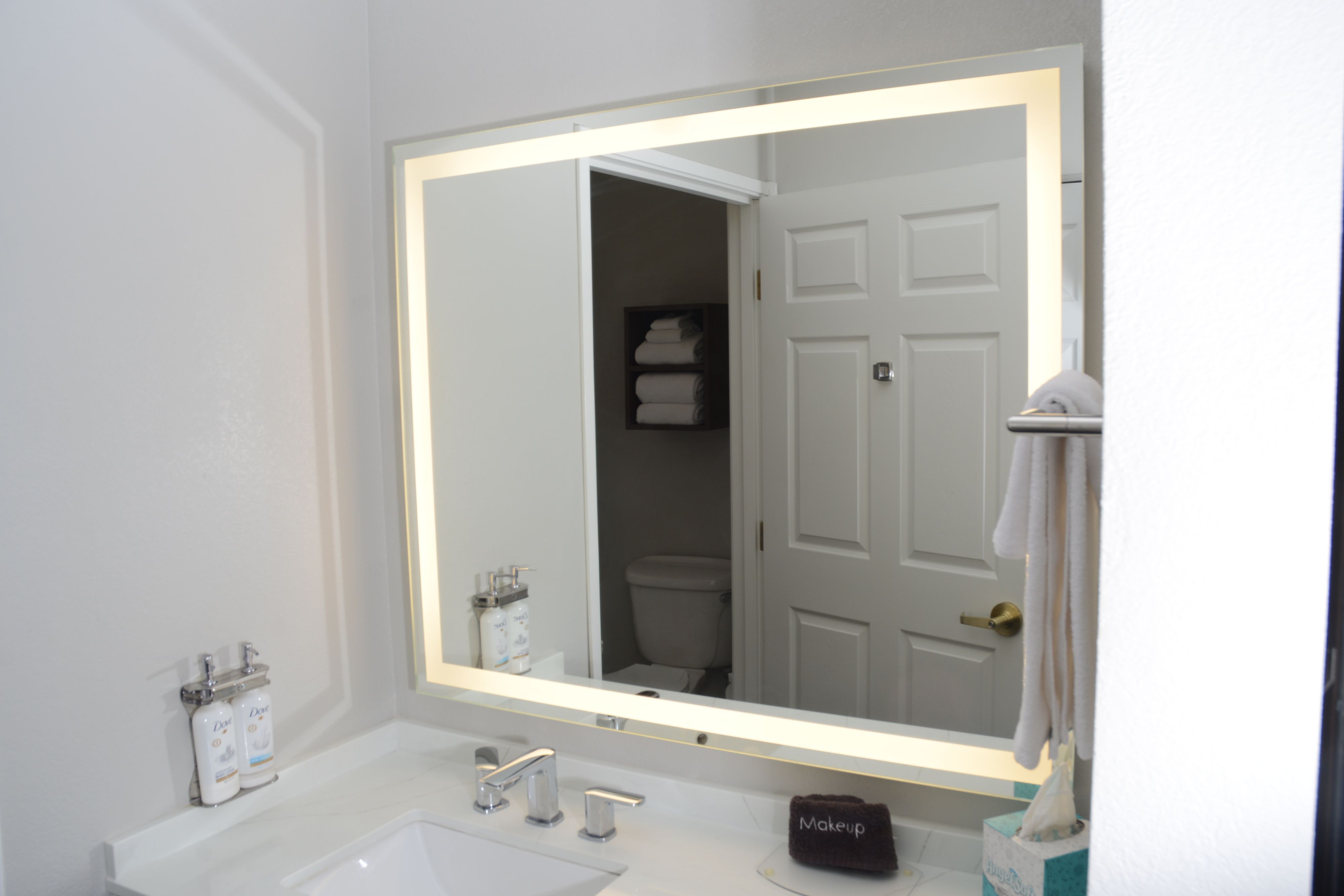 image Elegant bathroom featuring a backlit mirror and modern toiletries.