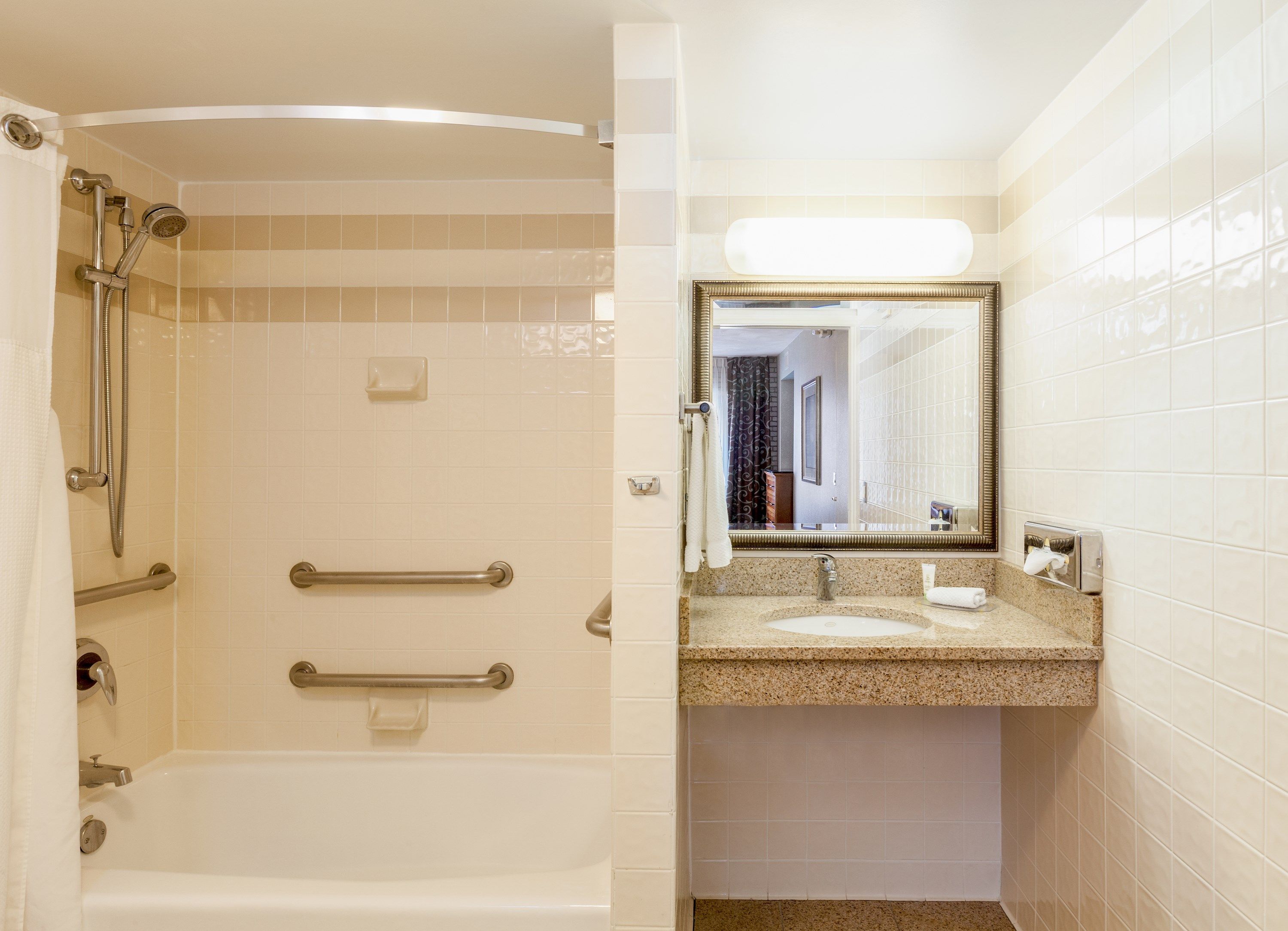 image Bathroom with a grab-bar-equipped tub, stone-finish vanity countertop, and silver-framed mirror