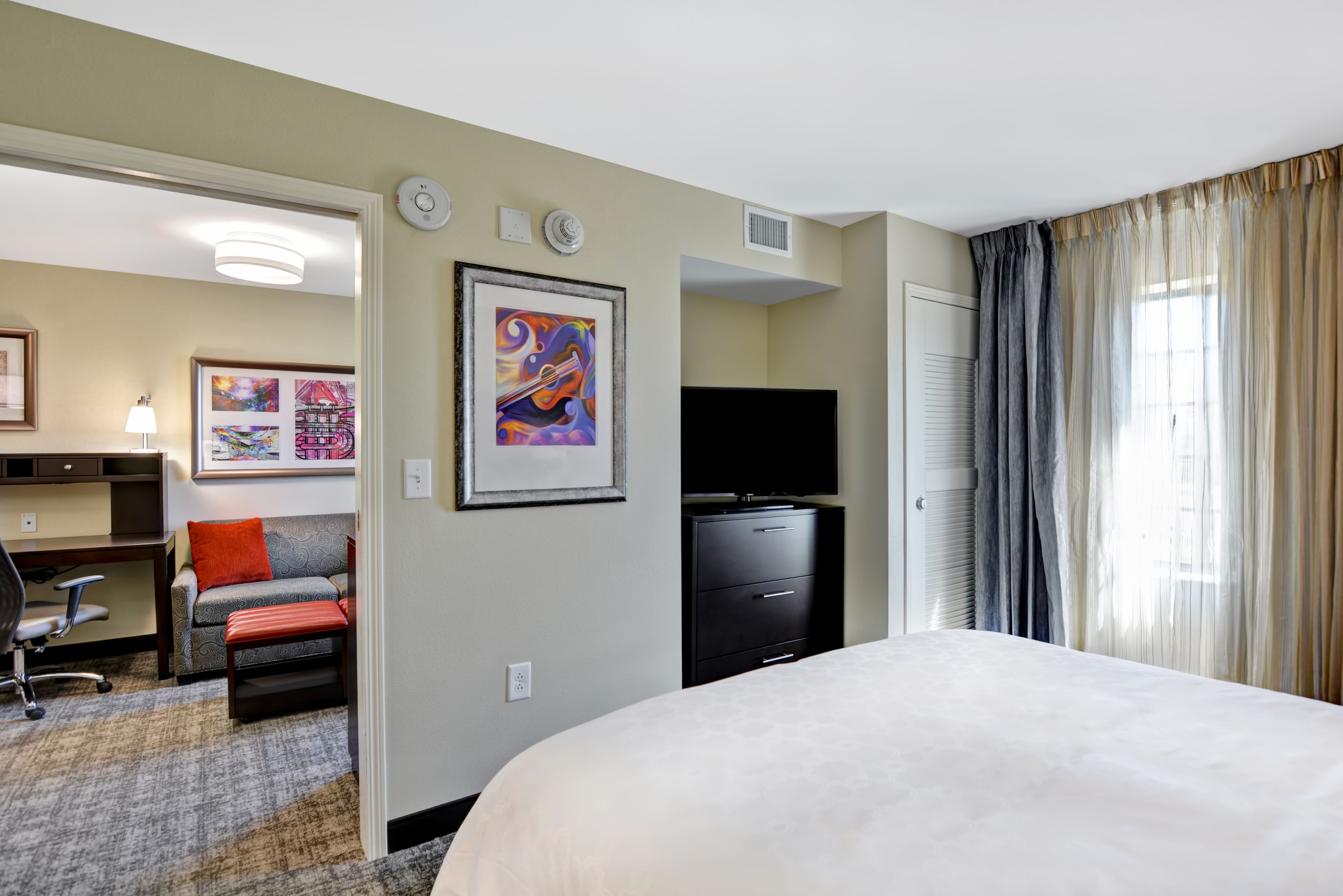image Bedroom with queen bed, desk, TV, and colorful artwork.