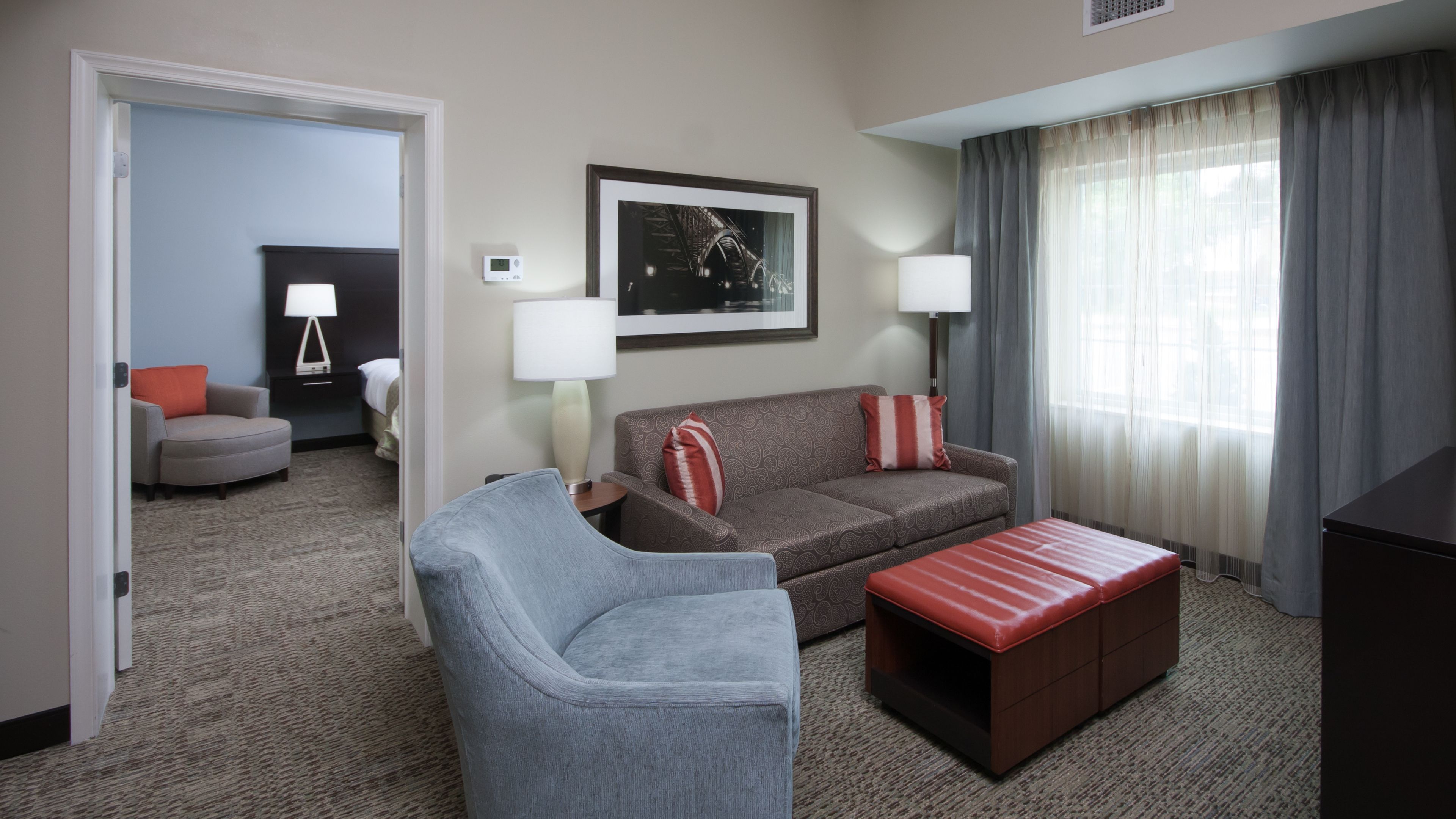 image Separate living room with two-tone seating and a red ottoman, opening through to the private bedroom