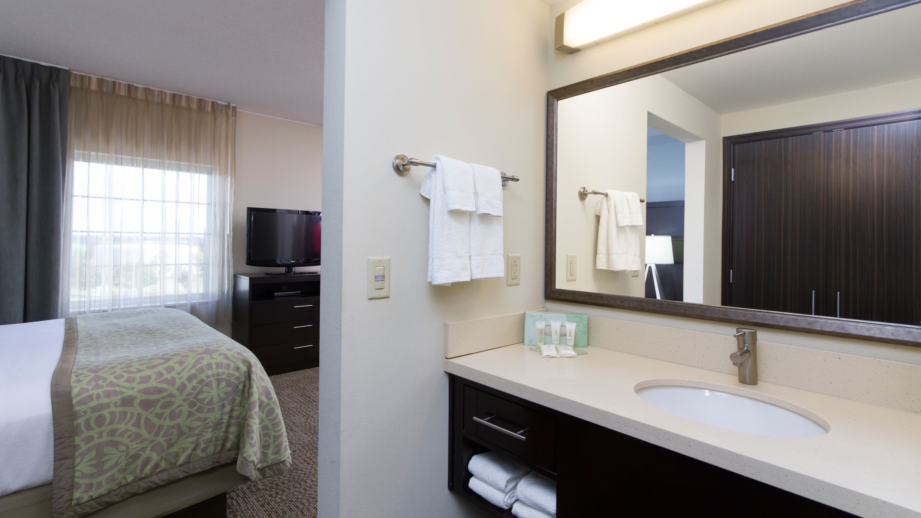 image Vanity with a wide mirror, dark wood cabinetry, and a glimpse of the king bed just steps away