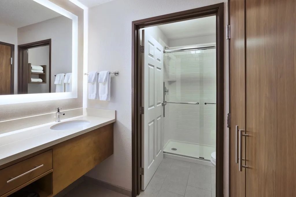 image Bathroom with sink, mirror, and shower area behind a door.