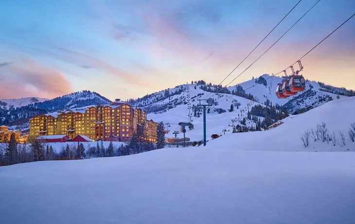 image Bathed in the soft hues of twilight, the Grand Summit Hotel emits a warm glow against the serene snowy mountains, while the gondolas ascend gracefully towards the peaks, promising exhilarating winter thrills.