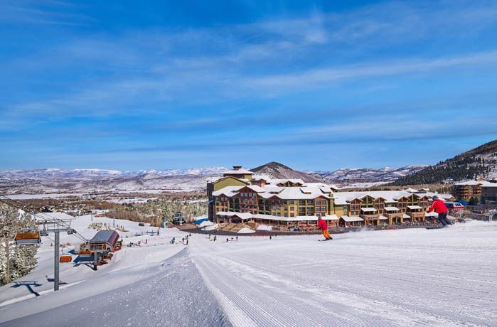 image As skiers carve their way down the freshly groomed slopes, the Grand Summit Hotel looms beautifully in the background, framed by a breathtaking winter landscape under a brilliant blue sky.