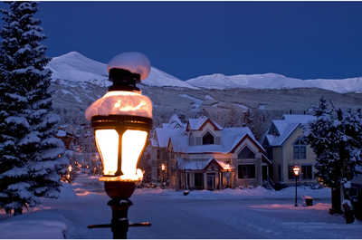 A snow-covered town square bathed in the soft glow of street lamps at dusk.