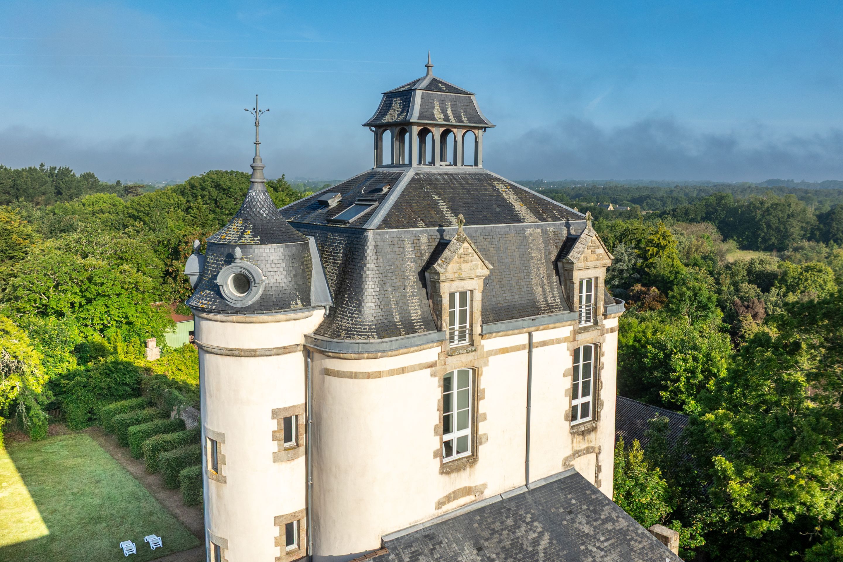 image The slate-roofed tower shows off its decorative stonework against a backdrop of greenery.