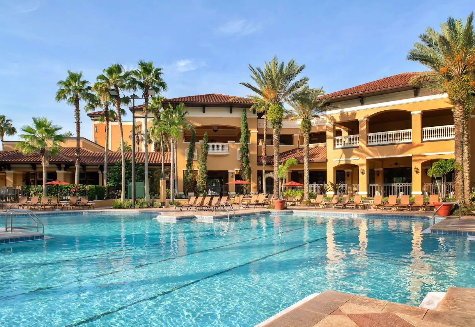image Spread out on a sun lounger along the pool deck, palms overhead and terracotta buildings on either side