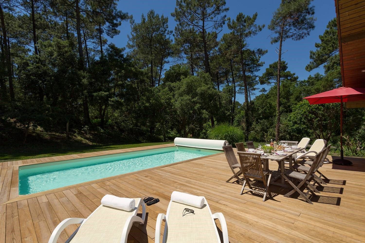 image Sunlit wooden deck with sun loungers, dining table, and a private pool — tall Landes pines framing the garden on all sides.