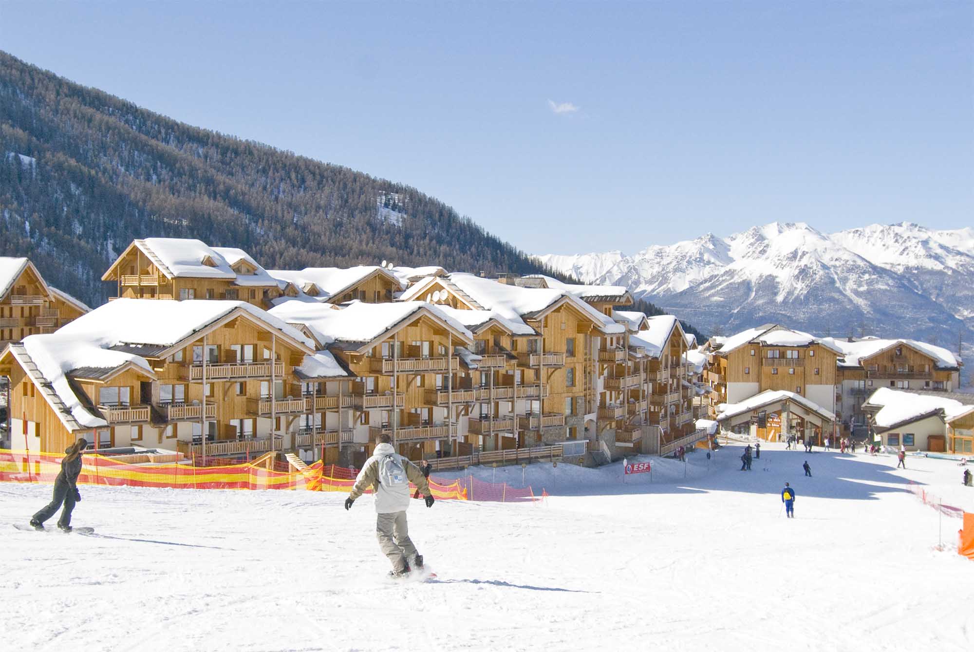 image Snowboarders on the slopes with wooden buildings and mountains behind