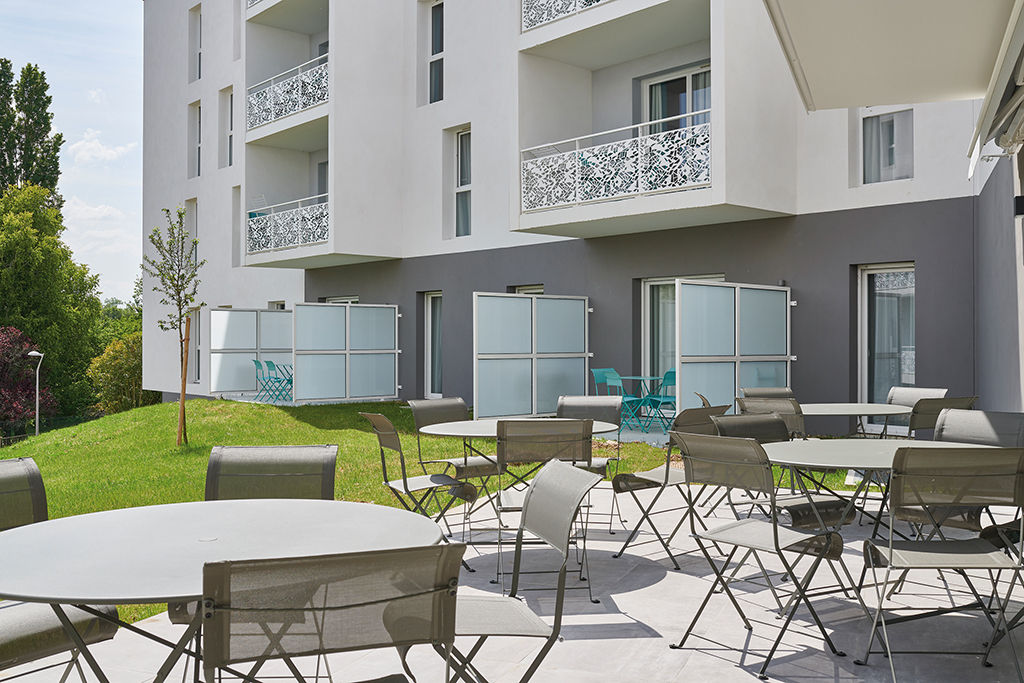 image Metal tables and chairs on the terrace look out over the green lawn and the apartment balconies