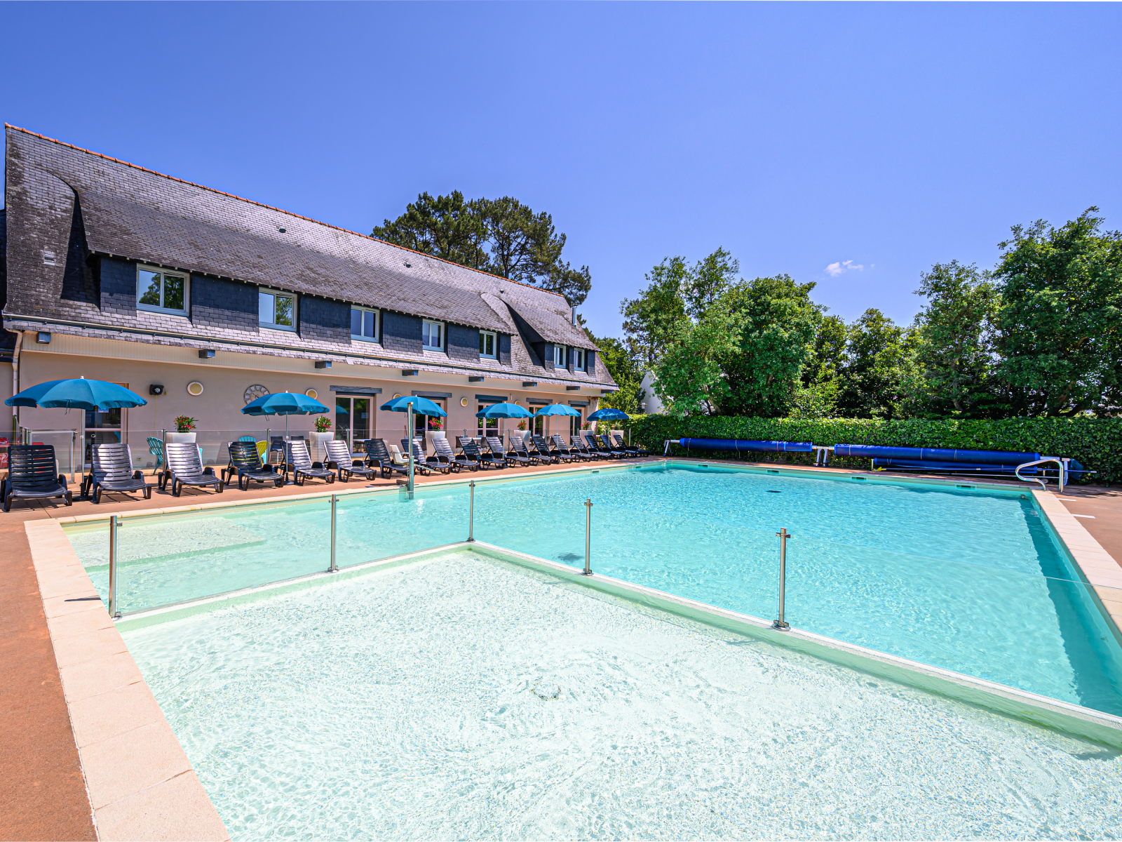image Shallow wading pool in the foreground behind a glass safety rail, with the main heated pool and lounger terrace beyond