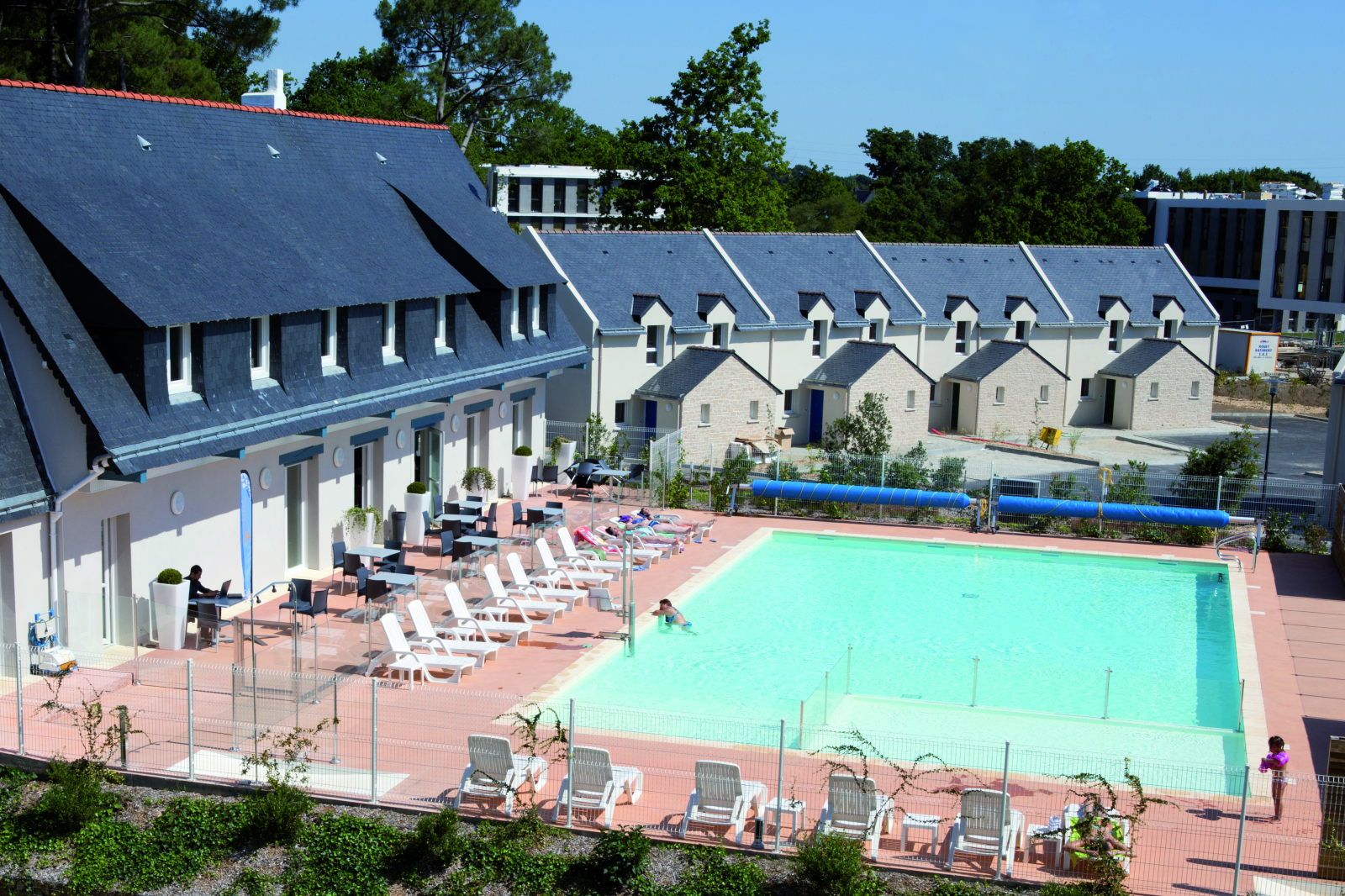 image Aerial view of the pool terrace with white loungers, café seating, and a row of Breton slate-roofed cottages behind