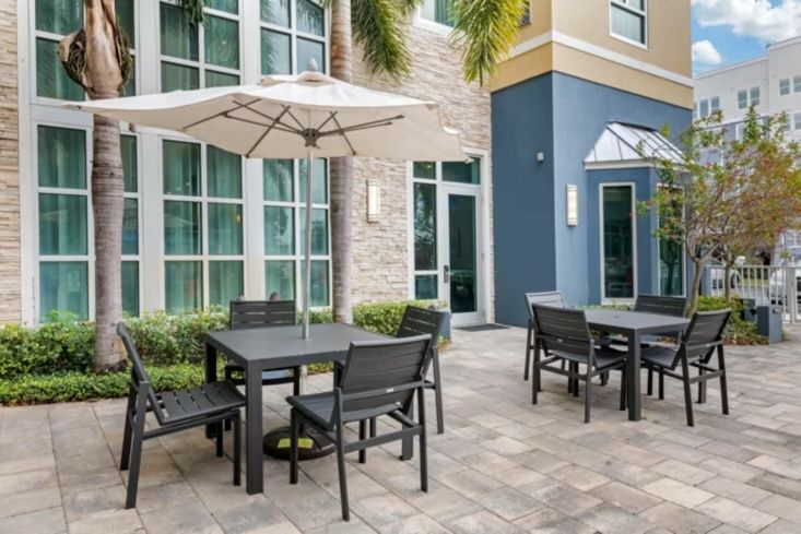 image Outdoor patio with metal tables, chairs, and white umbrellas beside a palm-lined wall