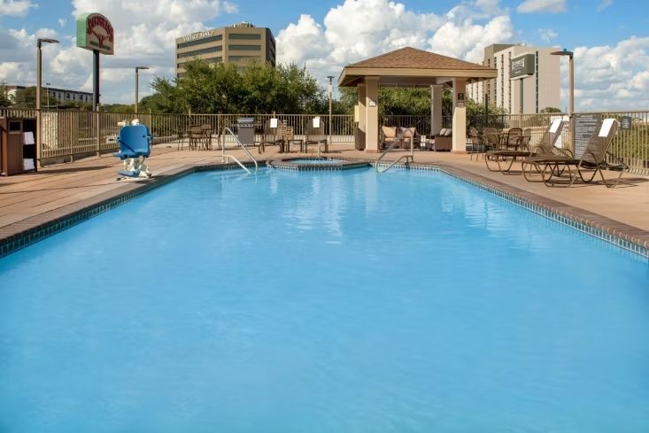 image Rectangular outdoor pool with brown lounge chairs and a shaded gazebo — open year-round