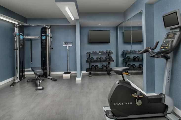image Light blue fitness room with a Matrix stationary bike, cable machine, dumbbell rack, and two wall-mounted TVs