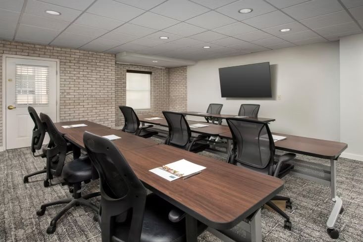 image Meeting room with boardroom-style dark wood tables, black office chairs, an exposed brick wall, and a wall-mounted TV