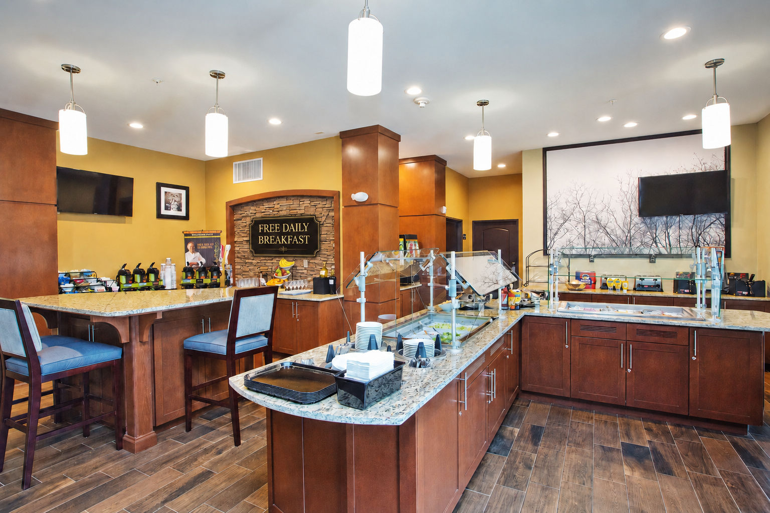 image On-site breakfast bar with hot food displays, bar seating, and a mounted TV.
