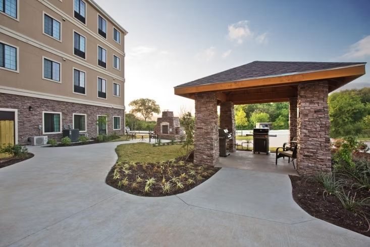 image Outdoor gazebo with a barbecue grill, landscaped grounds, and hotel building in the background.