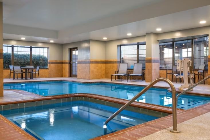 image Hot tub and pool deck bathed in natural light, with cushioned lounge chairs lined along the windows