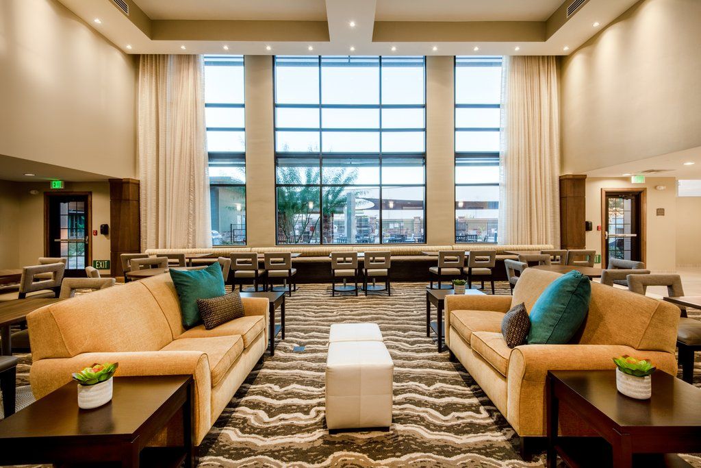 image Sunlit lobby with beige sofas, blue accent cushions, and a communal table for guests