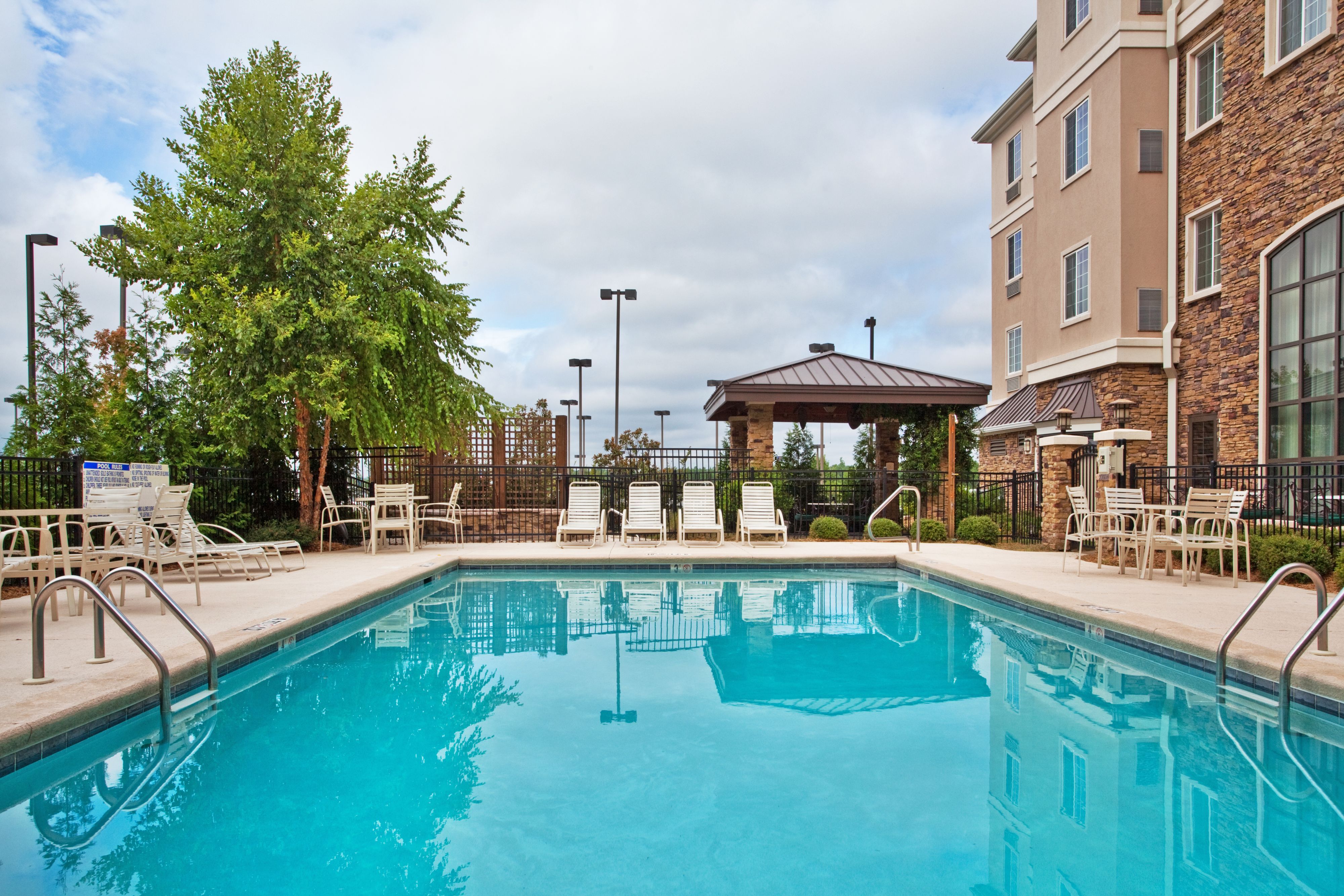 image Unwind by the sparkling pool surrounded by lush greenery and cozy lounge chairs.